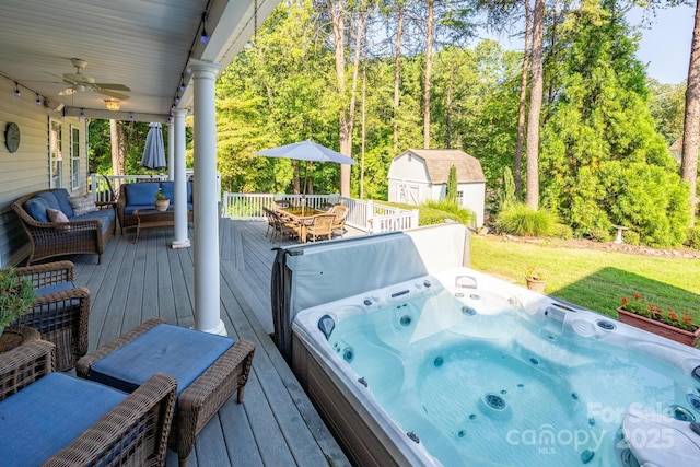 wooden deck with a storage unit, hot tub deck surround, a ceiling fan, outdoor dining space, and an outdoor structure