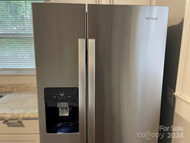 room details with white cabinets, stainless steel refrigerator with ice dispenser, and light stone countertops