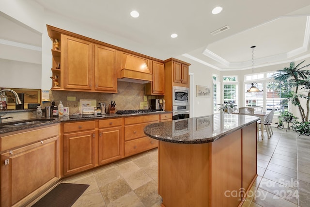 kitchen with a tray ceiling, gas stovetop, custom exhaust hood, backsplash, and a sink