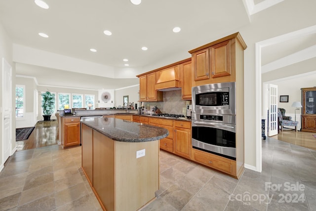 kitchen featuring appliances with stainless steel finishes, dark stone countertops, custom exhaust hood, a center island, and kitchen peninsula