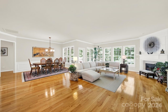 living room with visible vents, a glass covered fireplace, ornamental molding, light wood-style floors, and a notable chandelier