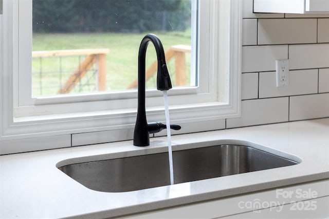 interior details featuring light stone countertops, tasteful backsplash, white cabinetry, and sink