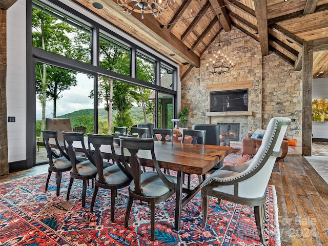 dining room with a stone fireplace, wood ceiling, a chandelier, high vaulted ceiling, and beamed ceiling