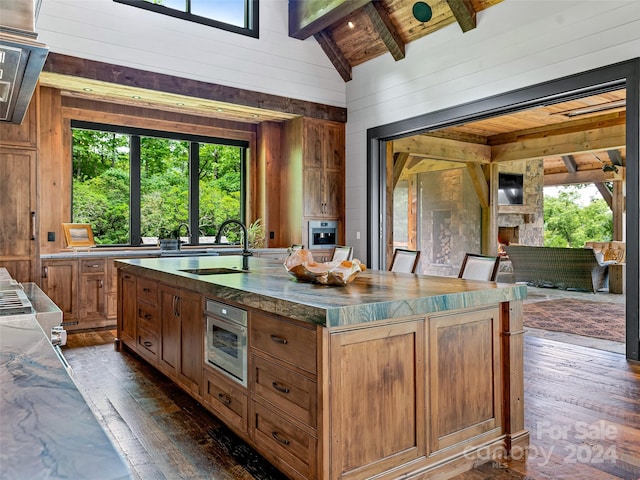 kitchen featuring sink, wood walls, wood ceiling, an island with sink, and beamed ceiling