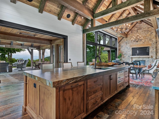 kitchen featuring dark wood-type flooring, sink, wooden ceiling, an island with sink, and beam ceiling