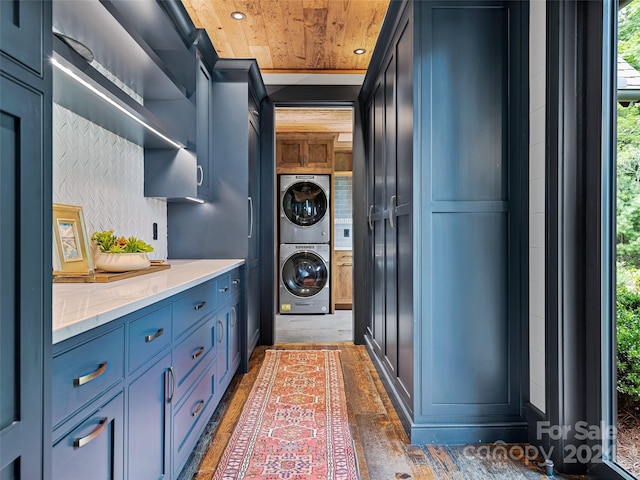 laundry area featuring cabinets, stacked washer and clothes dryer, dark wood-type flooring, and wooden ceiling