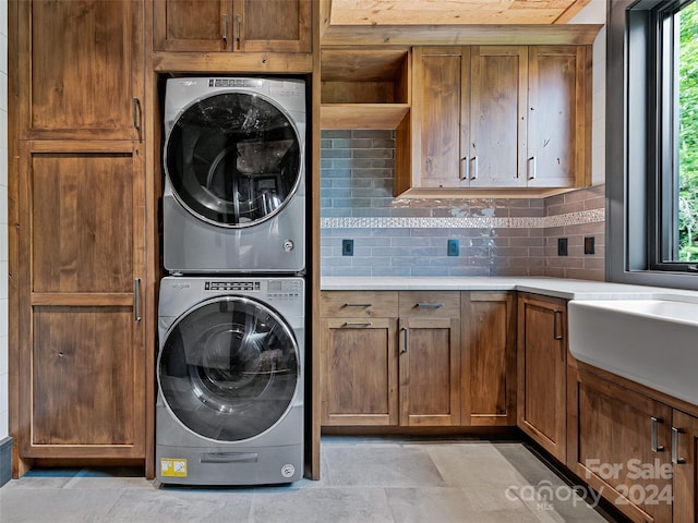 clothes washing area featuring sink, cabinets, and stacked washer / dryer