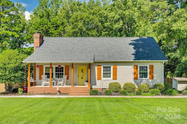 view of front of house with a porch, a front yard, and a storage shed