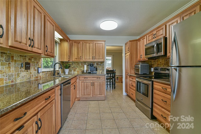 kitchen featuring sink, stainless steel appliances, ornamental molding, light tile patterned flooring, and dark stone counters