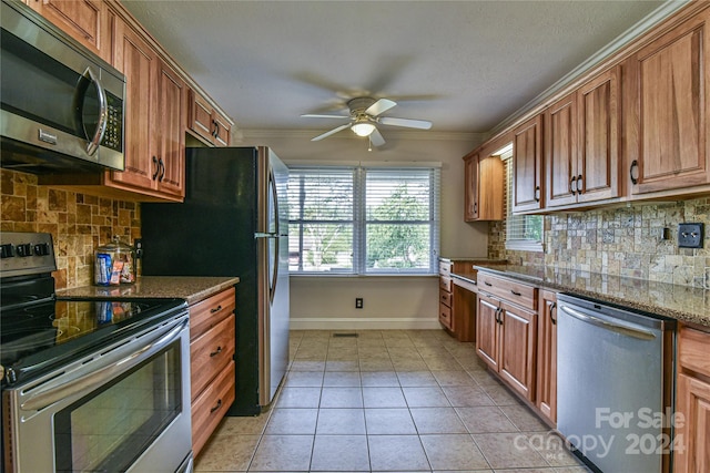 kitchen featuring ceiling fan, dark stone countertops, stainless steel appliances, ornamental molding, and light tile patterned flooring