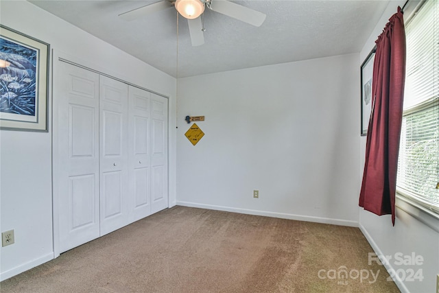 unfurnished bedroom with carpet flooring, a textured ceiling, ceiling fan, and a closet