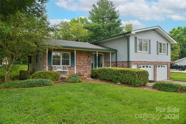 tri-level home featuring a front lawn, covered porch, and a garage