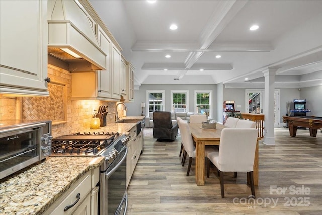 kitchen with cream cabinets, stainless steel gas range oven, light stone countertops, and custom exhaust hood