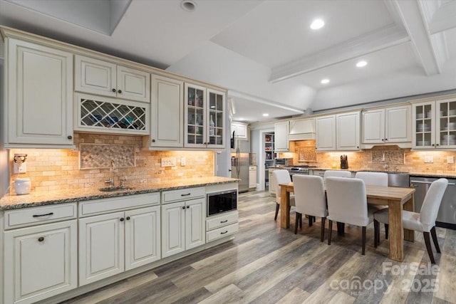 kitchen with appliances with stainless steel finishes, beam ceiling, sink, and light wood-type flooring