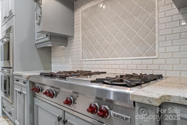 kitchen with light stone counters, stainless steel appliances, wall chimney exhaust hood, and tasteful backsplash