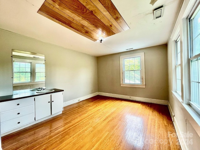 empty room with sink, plenty of natural light, wooden ceiling, and light wood-type flooring