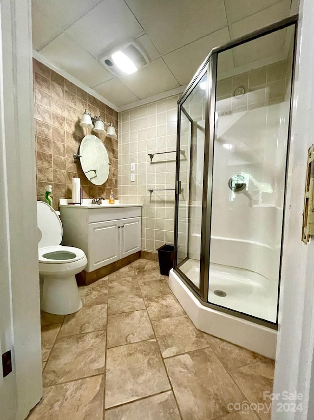 bathroom with vanity, toilet, tile walls, and a shower with shower door