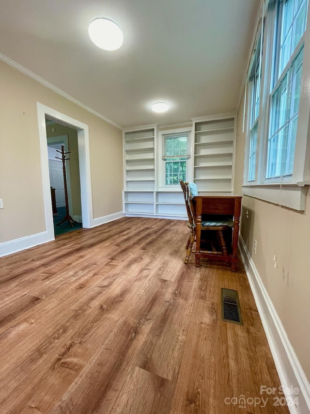 unfurnished dining area with built in shelves, ornamental molding, and wood-type flooring