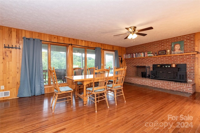 dining space featuring a fireplace, wooden walls, a textured ceiling, ceiling fan, and hardwood / wood-style flooring