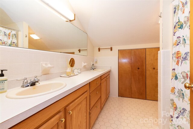 bathroom with lofted ceiling, tile walls, backsplash, and dual vanity