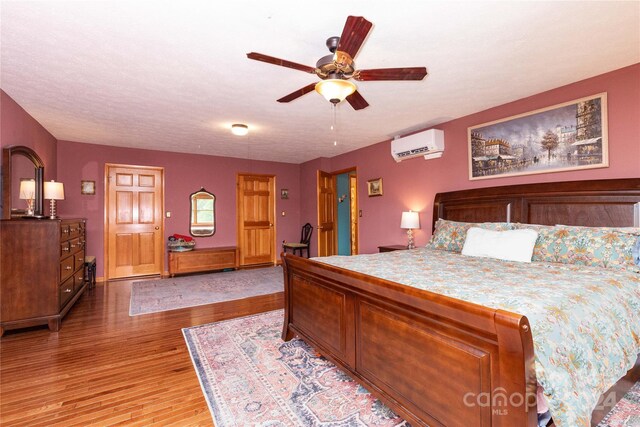 bedroom featuring light hardwood / wood-style flooring, ceiling fan, and an AC wall unit