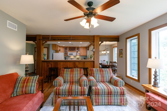 living area featuring ceiling fan with notable chandelier, wood-type flooring, visible vents, and baseboards