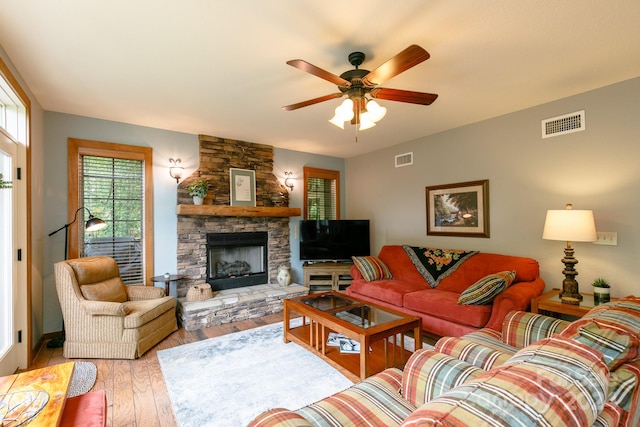 living room with a stone fireplace, light wood-type flooring, and ceiling fan