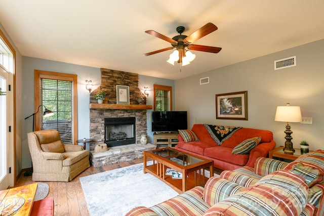 living room featuring light wood-style floors, ceiling fan, a fireplace, and visible vents