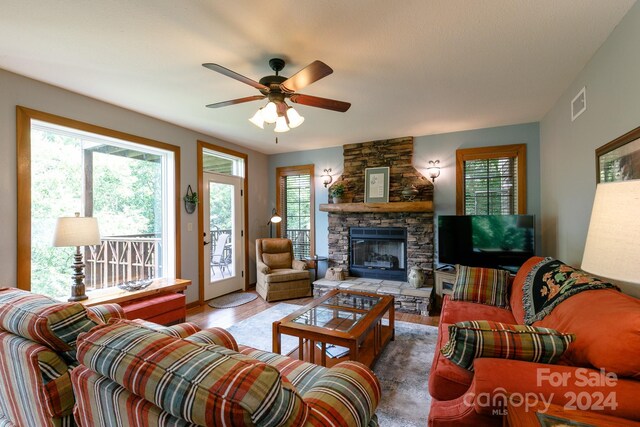 living room featuring a stone fireplace, a wealth of natural light, and ceiling fan