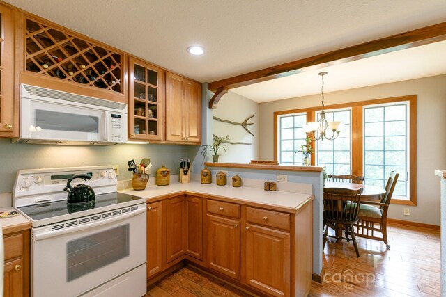 kitchen with a notable chandelier, white appliances, kitchen peninsula, hanging light fixtures, and hardwood / wood-style floors