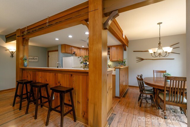 kitchen featuring white refrigerator, an inviting chandelier, kitchen peninsula, light hardwood / wood-style floors, and decorative light fixtures