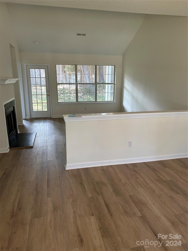 unfurnished living room featuring a textured ceiling, dark hardwood / wood-style flooring, and lofted ceiling