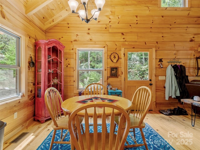 dining space featuring light hardwood / wood-style floors, vaulted ceiling with beams, an inviting chandelier, and wood walls