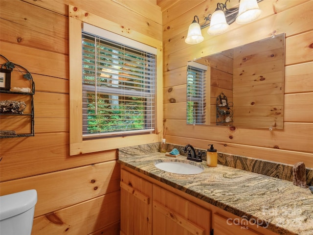 bathroom featuring vanity, wooden walls, and toilet