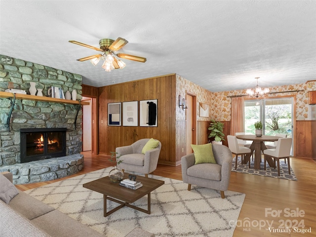 living room featuring light hardwood / wood-style floors, a fireplace, a textured ceiling, wooden walls, and ceiling fan with notable chandelier