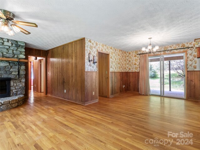 unfurnished living room featuring wood walls, a fireplace, light hardwood / wood-style floors, ceiling fan with notable chandelier, and a textured ceiling