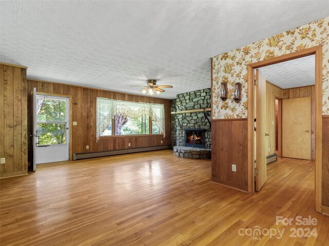 unfurnished living room featuring a fireplace, light hardwood / wood-style floors, a baseboard heating unit, a textured ceiling, and wooden walls