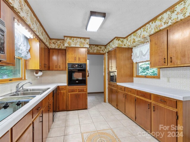 kitchen with light tile patterned floors, sink, a textured ceiling, black appliances, and crown molding