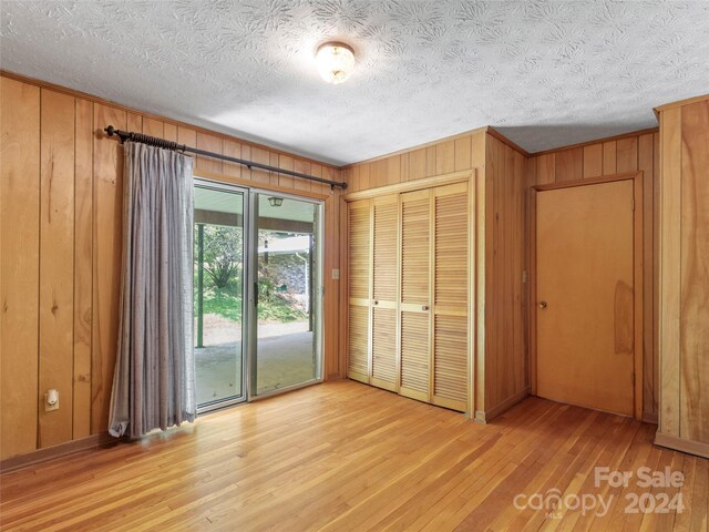 unfurnished bedroom with access to exterior, a closet, wood walls, and light hardwood / wood-style floors