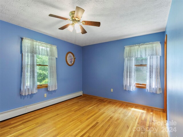 empty room with ceiling fan, light hardwood / wood-style flooring, a baseboard radiator, and a textured ceiling