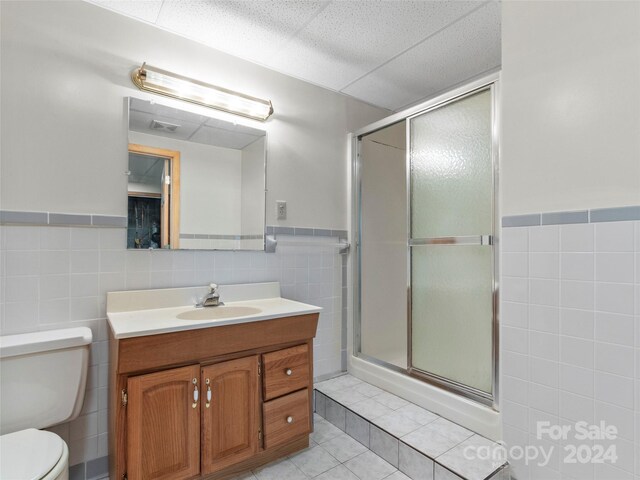 bathroom with toilet, vanity, tile walls, tile patterned floors, and a shower with shower door