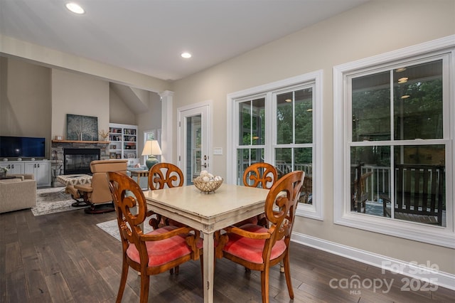 dining space featuring decorative columns, a fireplace, and dark wood-type flooring