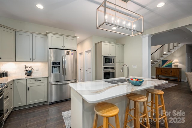 kitchen with sink, stainless steel appliances, light stone counters, dark hardwood / wood-style flooring, and a center island with sink