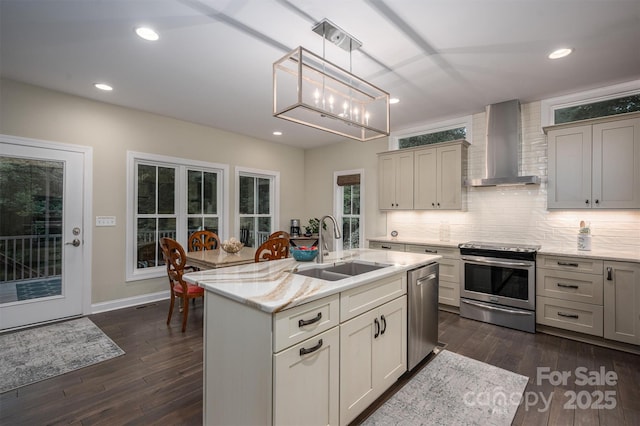 kitchen with stainless steel appliances, a kitchen island with sink, sink, wall chimney range hood, and decorative light fixtures