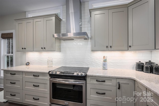 kitchen featuring gray cabinetry, light stone countertops, wall chimney range hood, electric stove, and decorative backsplash