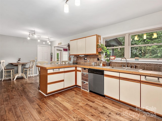 kitchen with sink, stainless steel dishwasher, kitchen peninsula, white cabinets, and backsplash