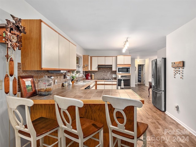 kitchen featuring sink, stainless steel appliances, tile counters, decorative backsplash, and kitchen peninsula