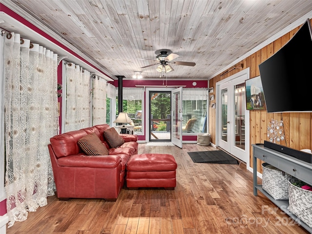 living room featuring wood walls, a wood stove, hardwood / wood-style flooring, crown molding, and french doors