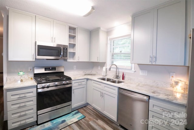 kitchen featuring light stone counters, appliances with stainless steel finishes, wood finished floors, open shelves, and a sink