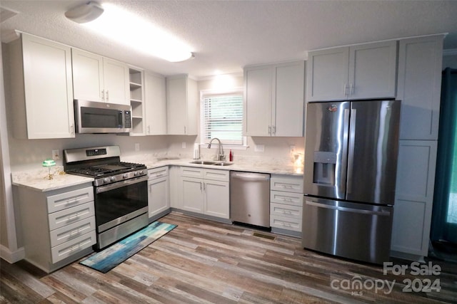 kitchen featuring open shelves, stainless steel appliances, a sink, a textured ceiling, and wood finished floors